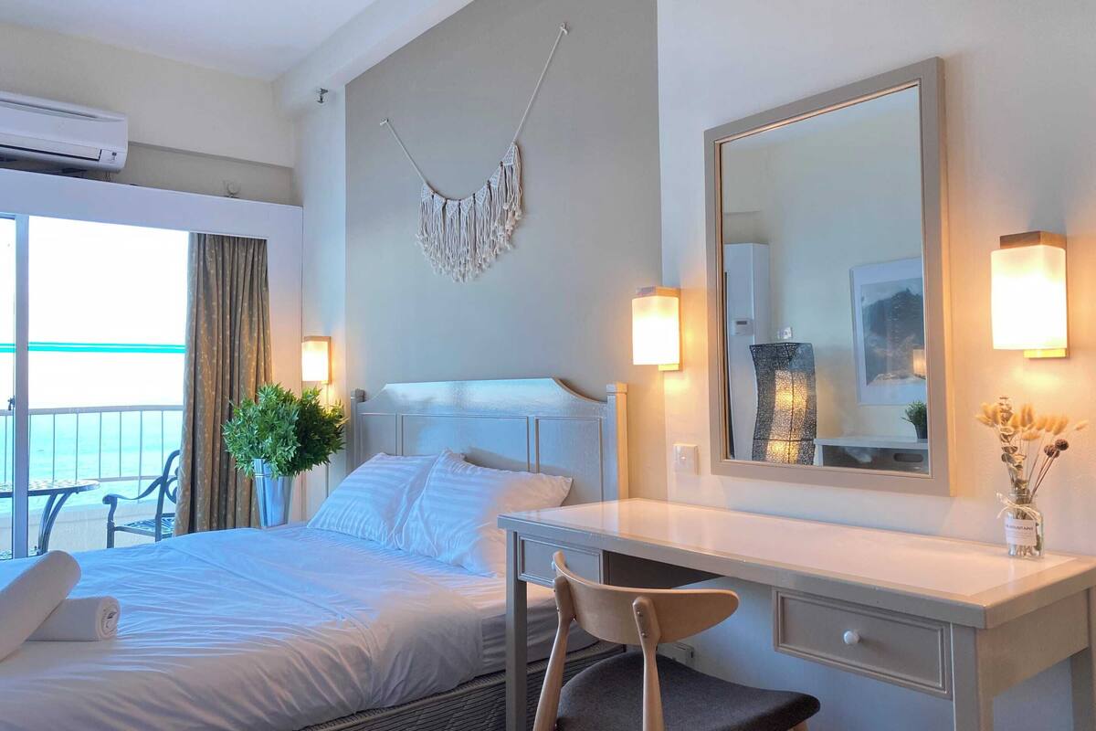 A hotel room with a bed, bedside table, chair, and a large mirror.