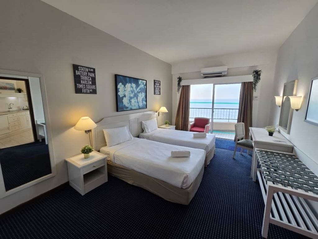 Une chambre d’hôtel avec deux lits, un bureau, une chaise et une vue sur l’océan.