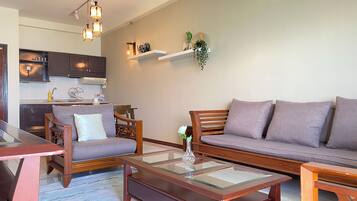 A living room with a sofa, armchairs, a coffee table, and a kitchen area in the background.