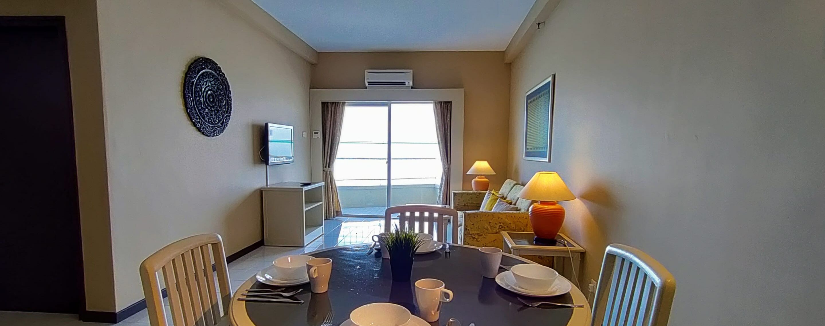 A dining area with a table set for four, a TV, and a window with curtains.