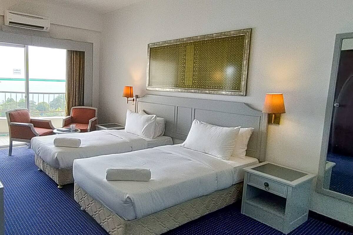 A hotel room with two beds, a large window, a chair, and a wall-mounted artwork.