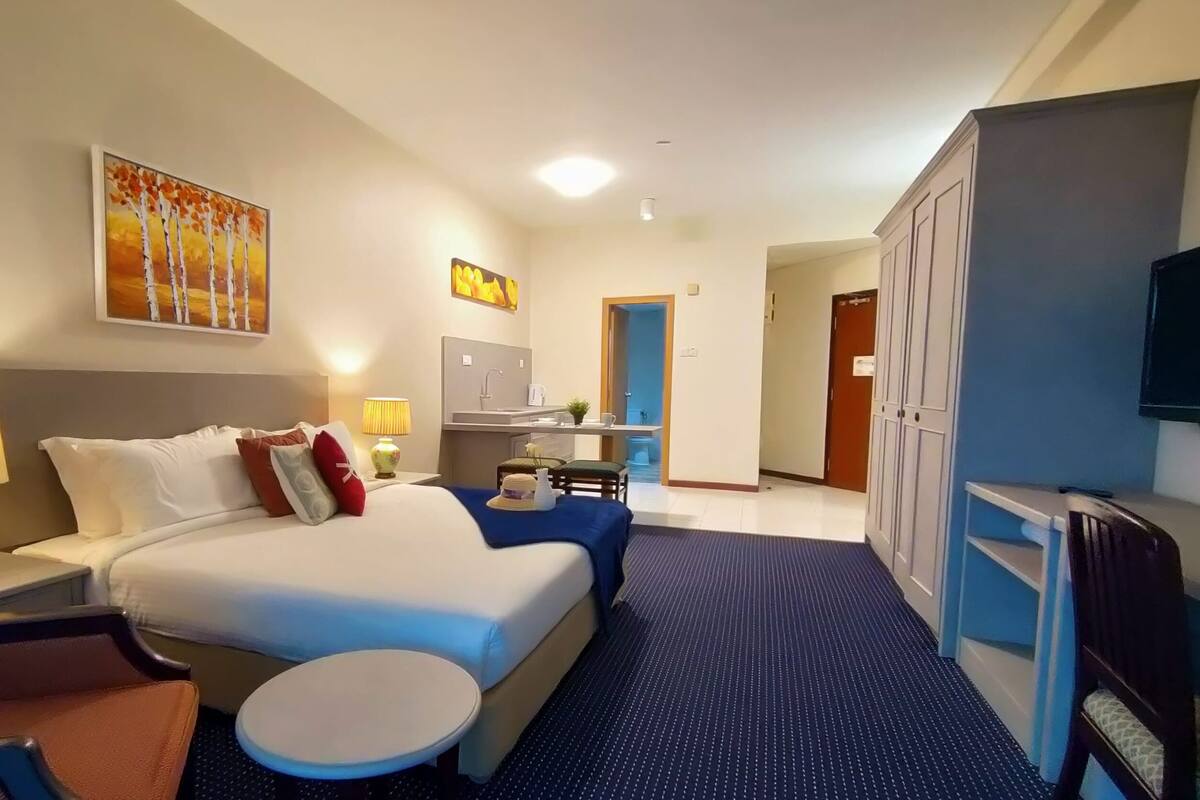 A hotel room with a bed, bedside tables, a round table, a TV, and a kitchenette.