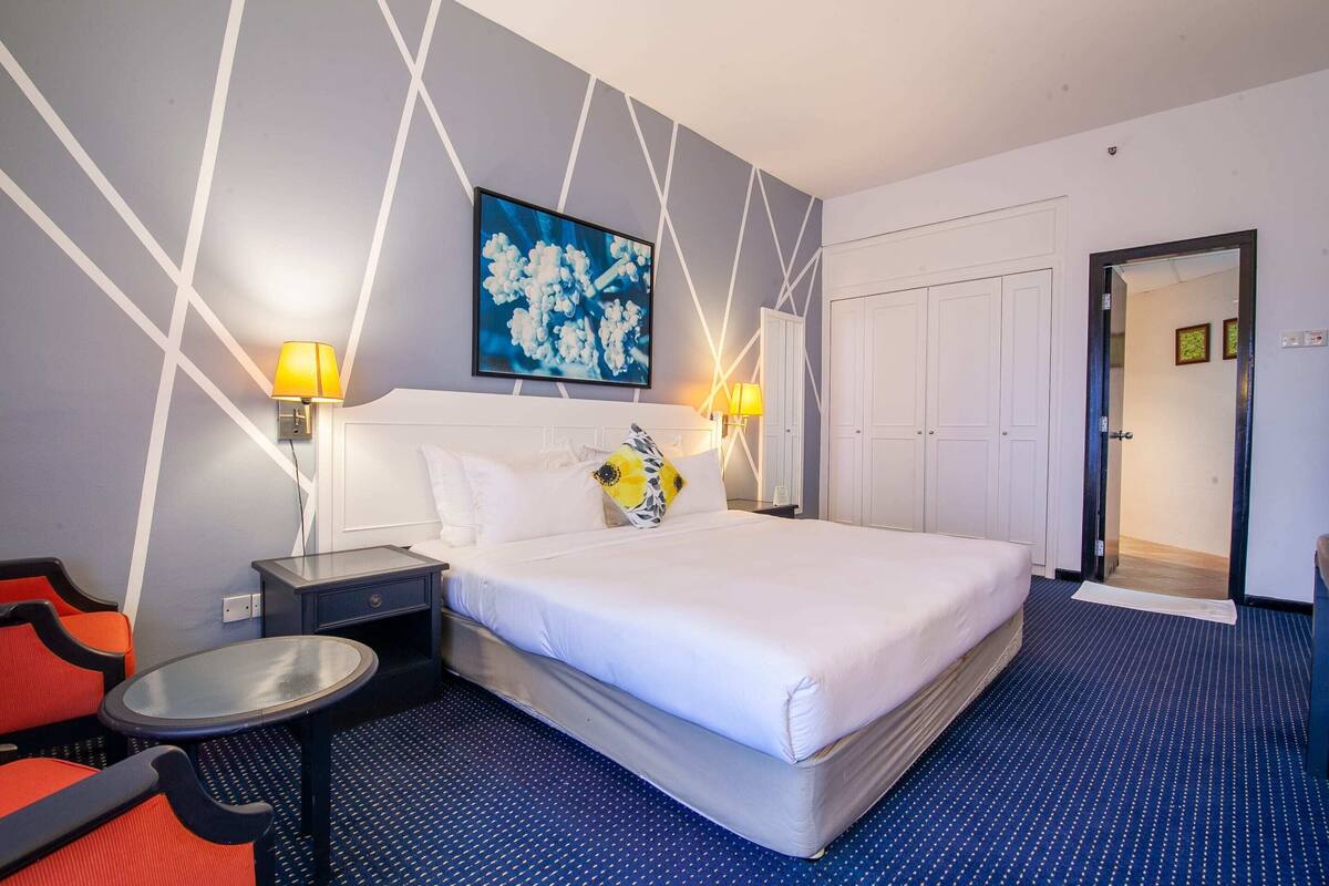 A hotel room with a large bed, two bedside tables with lamps, a small round table, and a chair.