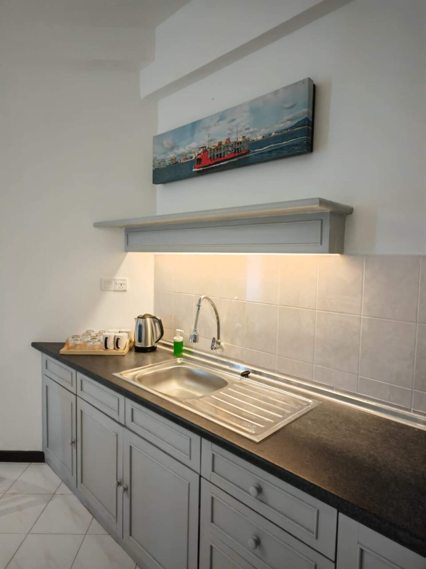 A modern kitchen with a stainless steel sink, grey cabinets, and a painting above the countertop.