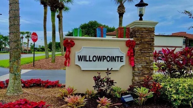 Señal de Willow Pointe con una señal de parada cerca, rodeada de plantas ajardinadas y palmeras.