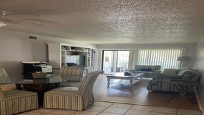 Un salón espacioso con una mesa de comedor de cristal, sillones a rayas, un sofá y un televisor.