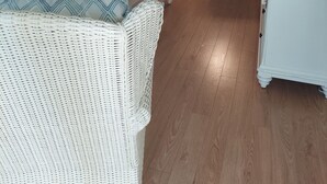 Una sala de estar con un sofá, una mesa de centro y una silla de mimbre. Hay una zona de comedor con una silla y una mesa.