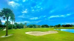 Un campo de golf con un estanque, palmeras y un cielo azul despejado.