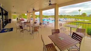 Un patio al aire libre con mesas y sillas, una piscina al fondo y vistas del paisaje circundante.