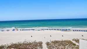 En strand med rækker af blå parasoller og strandstole, sandstrand og udsigt til havet.