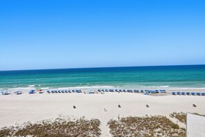 Una playa con hileras de sombrillas azules y sillas, arena y vista al océano.