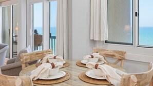 Spiseområde med et bord dækket til fire, med balkon og udsigt over havet.