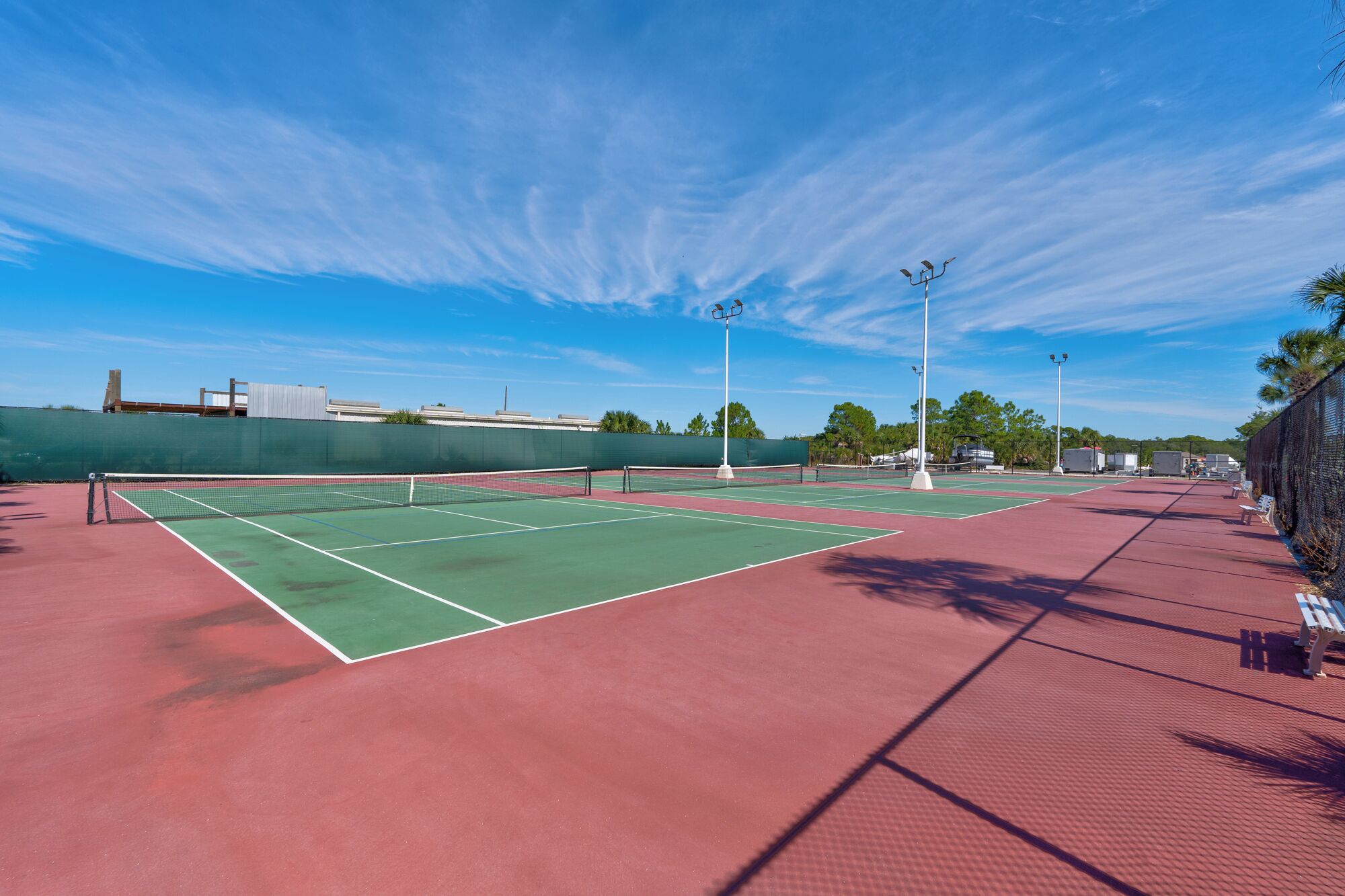 A tennis court with a net, green and red playing surfaces, and surrounding fencing.