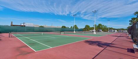 A tennis court with a net, green and red playing surfaces, and surrounding fencing.