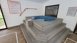 Un bain à remous accessible par des marches, doté d’une rambarde en bois et d’un panneau indiquant les règles à respecter.
