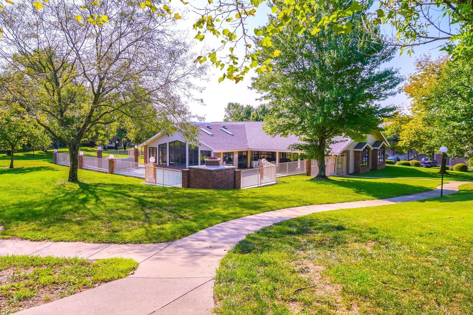 A residential building with a covered patio area, surrounded by well-maintained lawns and trees.
