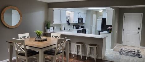 A modern kitchen with white cabinets, a wooden dining table with four chairs, and a small island with stools.