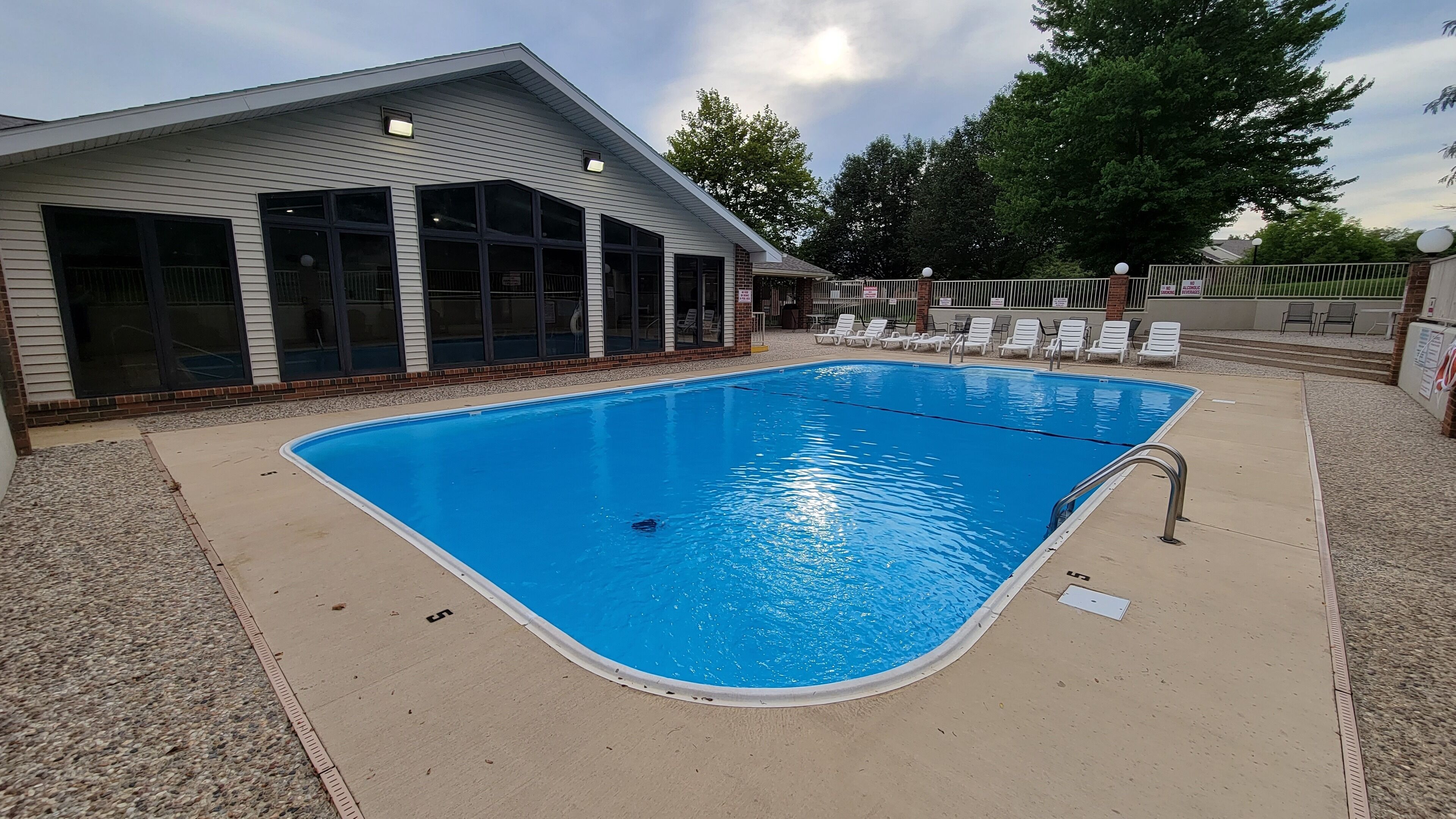 A rectangular swimming pool with a tiled deck, surrounded by a fence and lounge chairs.