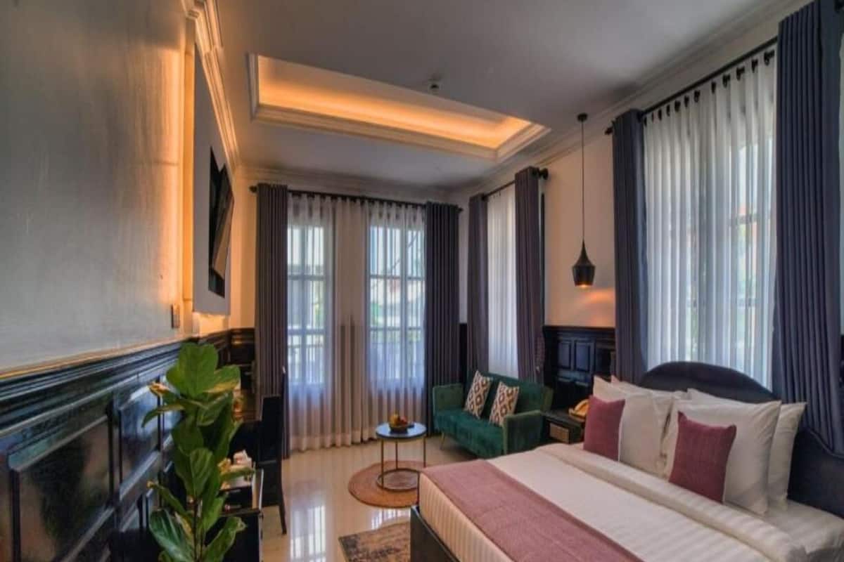 A spacious hotel room with a large bed, a seating area with a sofa and armchairs, a small side table, and a potted plant.