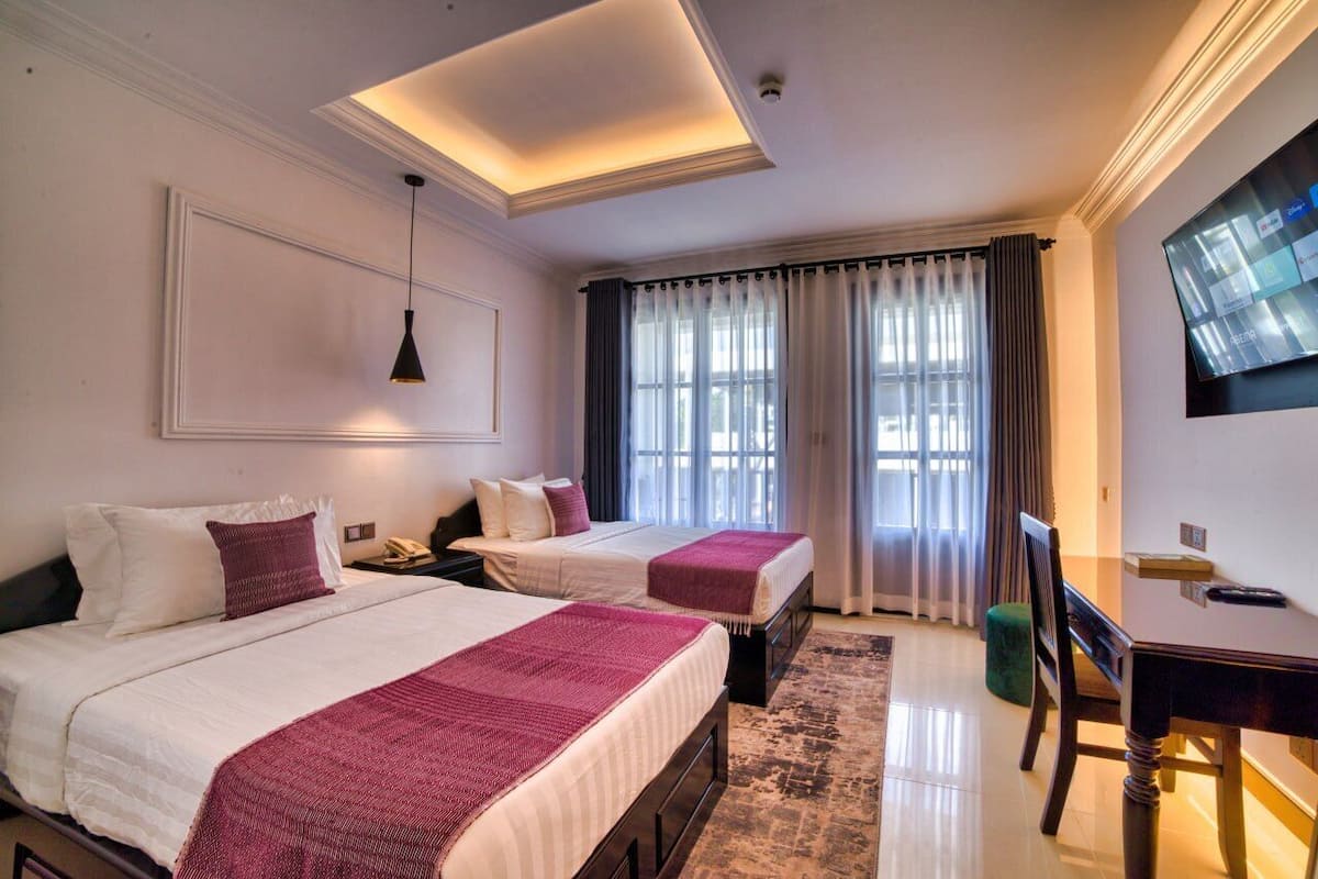 A hotel room with two beds, a desk, a chair, a television, and a large window with curtains.