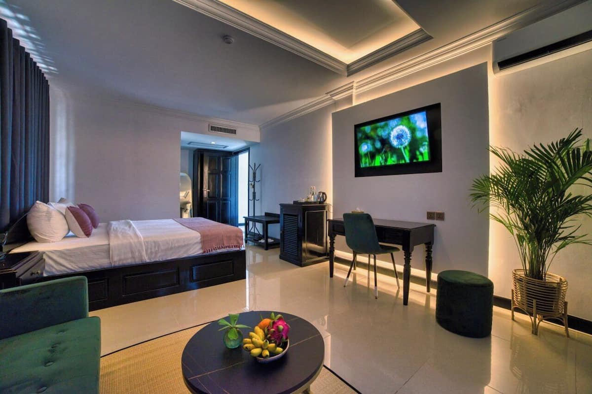 A modern hotel room with a bed, a desk, a television, and a dining area with a table and chairs.