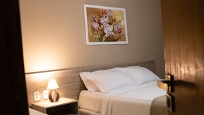 A hotel room with a bed, a bedside table with a lamp, and a painting on the wall. - Pousada Porto Prime (Sao Joao Da Barra)