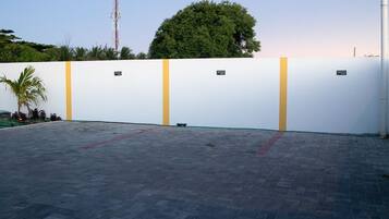 A paved outdoor area with a white wall featuring yellow vertical stripes and small plaques.