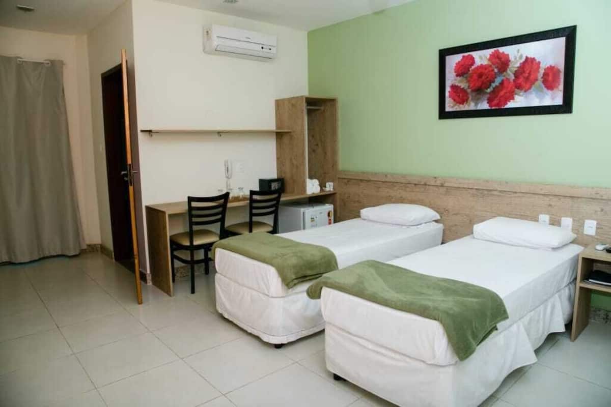 A hotel room with two beds, a desk, a chair, and a wardrobe.