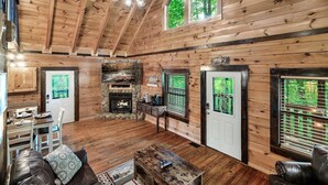 A log cabin interior with a dining area, a fireplace, and a large window overlooking greenery. - Free Dollywood Tix/VIEWS/Secluded/Couples/HotTub/ (Sevierville)