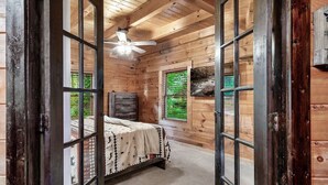 A wooden cabin bedroom with a bed, a ceiling fan, and a window with a view of greenery. - Free Dollywood Tix/VIEWS/Secluded/Couples/HotTub/ (Sevierville)