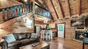 A spacious living area with a wooden staircase, a fireplace, a dining area, and a kitchen. - Free Dollywood Tix/VIEWS/Secluded/Couples/HotTub/ (Sevierville)