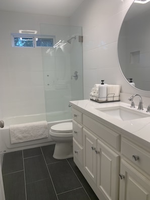 Une salle de bain moderne avec une douche à parois de verre, des toilettes blanches, un meuble-lavabo et un grand miroir.