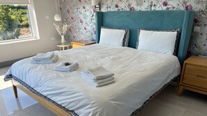 Ein ordentlich bezogenes Bett mit weißen Leinen und Handtüchern, einem türkisfarbenen Kopfteil und Blumenpapier.