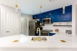Eine moderne Küche mit weißen Arbeitsplatten, blauen Schränken, Edelstahlgeräten und goldenen Armaturen.