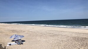A beach with a clear sky, a sandy shore, and a person sitting under a patterned umbrella. - Unbelievable October Deals - Booking through 10/31/26 (Davis Park)