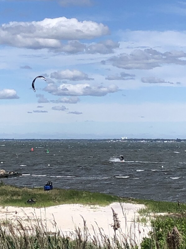Ein Strand mit Blick auf das Meer, ein Parasegel in der Ferne und ein Boot auf dem Wasser.