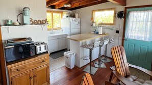 A compact kitchen with wooden cabinets, a microwave, toaster, and a refrigerator. There is a dining area with a wooden table and chairs, and a green door. - Unbelievable October Deals - Booking through 10/31/26 (Davis Park)
