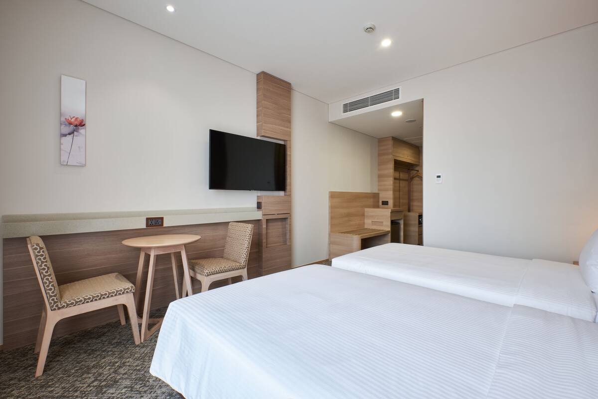 A hotel room with a bed, a desk, a chair, a television, and a small table.