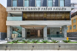 A modern hotel entrance with a glass facade, a name sign, and a covered entrance area.