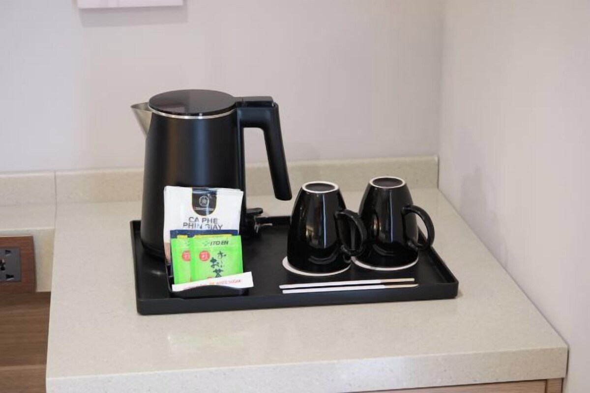 En kaffestation med en svart kaffebryggare, två svarta koppar och ett paket kaffekapslar på en bänkskiva.