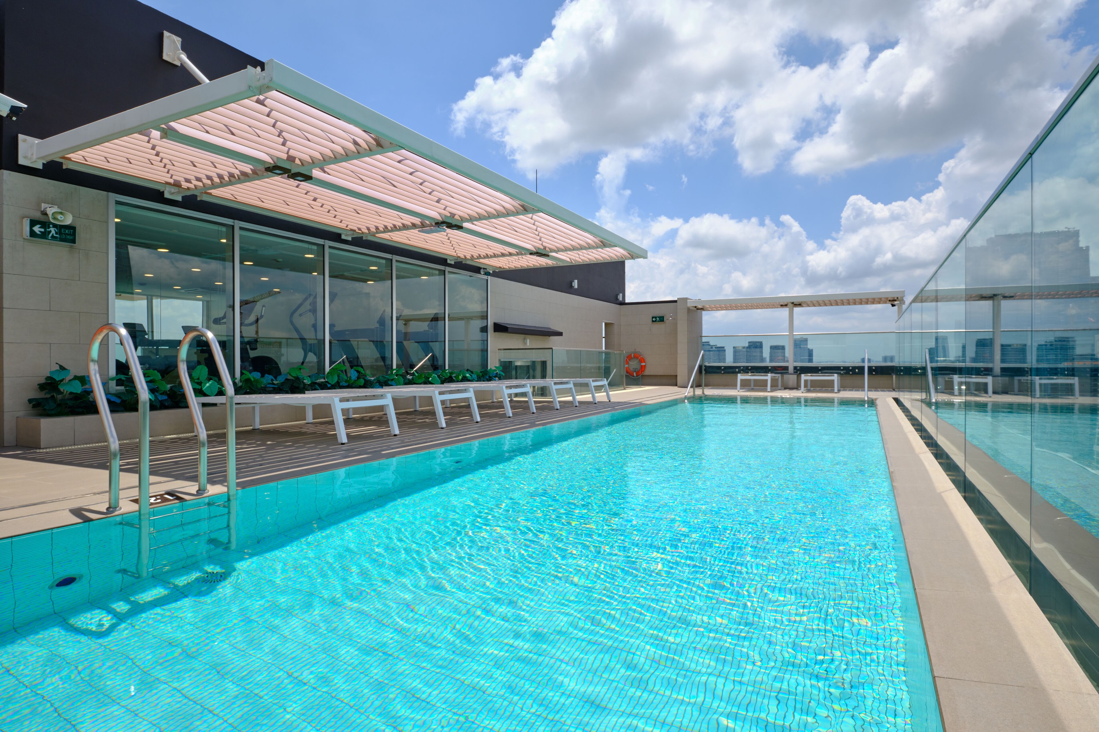 Une piscine intérieure moderne, avec une eau d’un bleu cristallin, des murs en verre et une vue sur la ville.