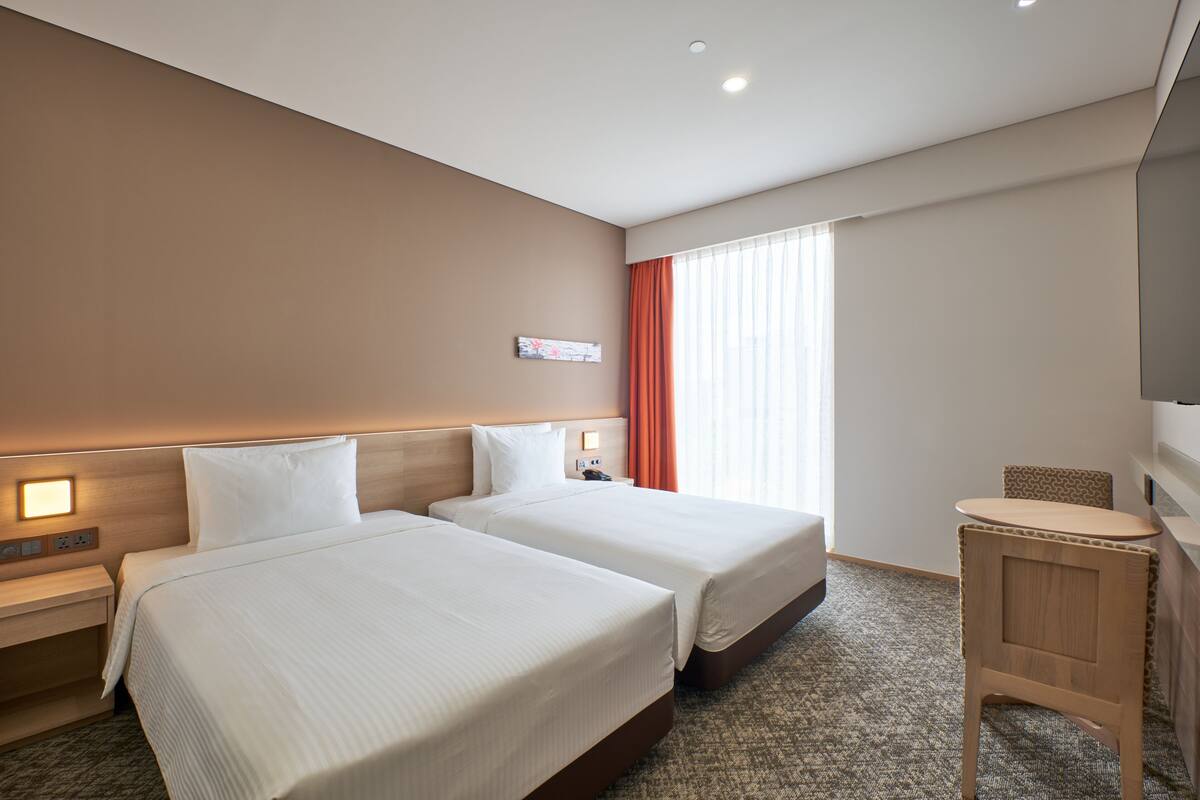 A hotel room with two beds, a small desk, a chair, and a television.
