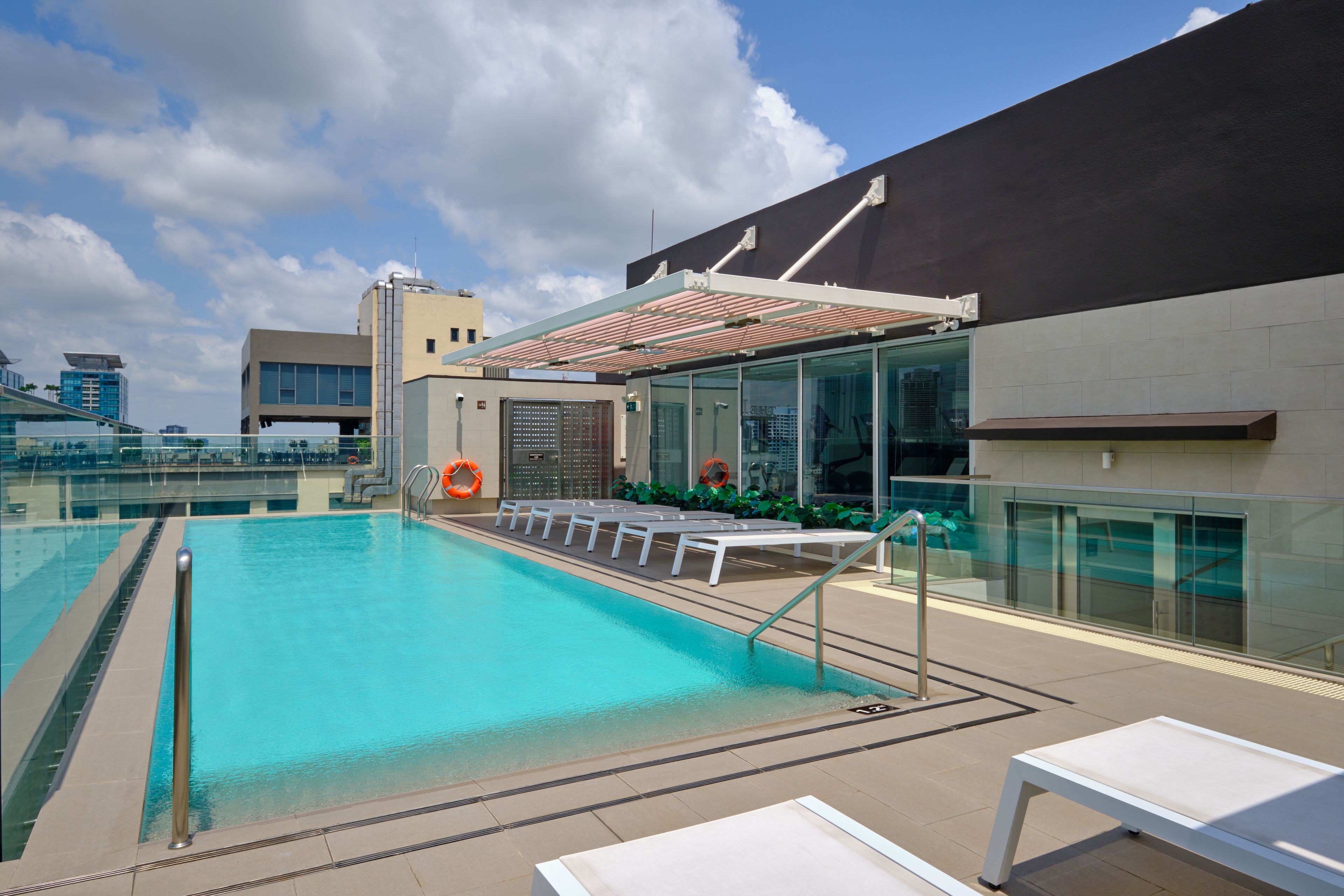 A rooftop swimming pool with lounge chairs and a glass railing.