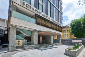 Une entrée d’hôtel moderne, avec une enseigne bien visible, un espace d’entrée abrité et un espace extérieur aménagé.