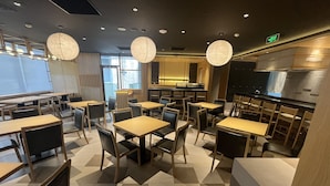 A modern restaurant interior with wooden tables and chairs, pendant lighting, and a visible kitchen area. - Sotetsu Grand Fresa Saigon (Ho Chi Minh City)