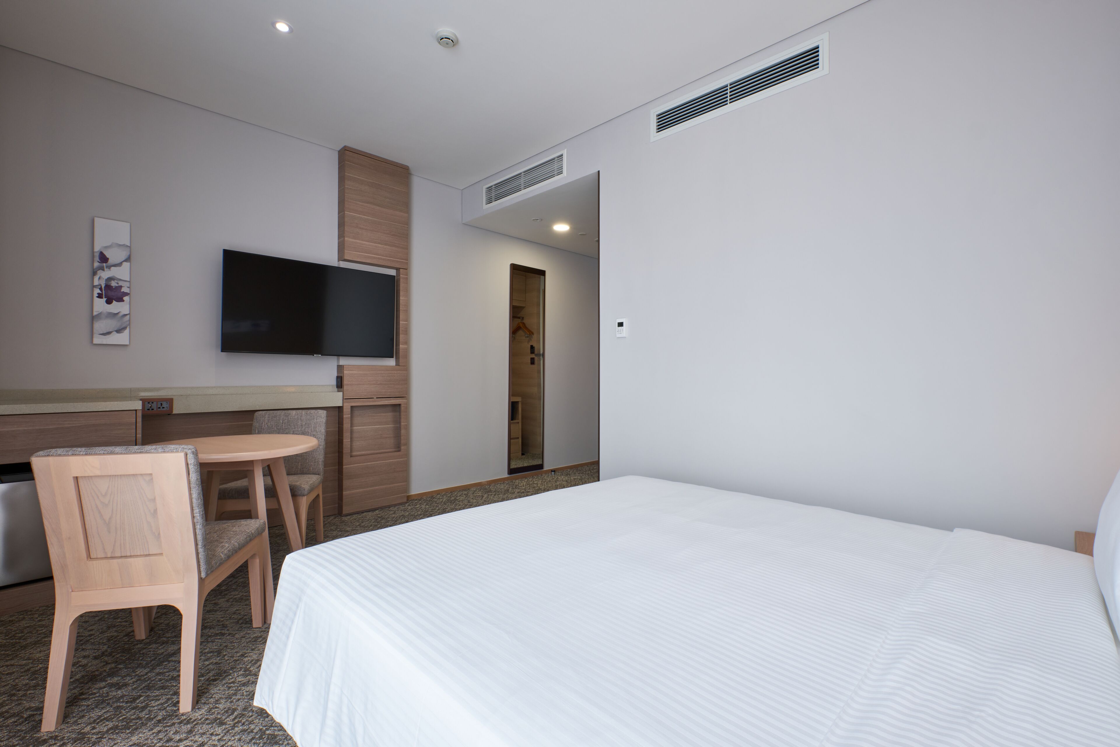 A hotel room with a bed, a TV mounted on the wall, a desk with a chair, and a door leading to a bathroom.