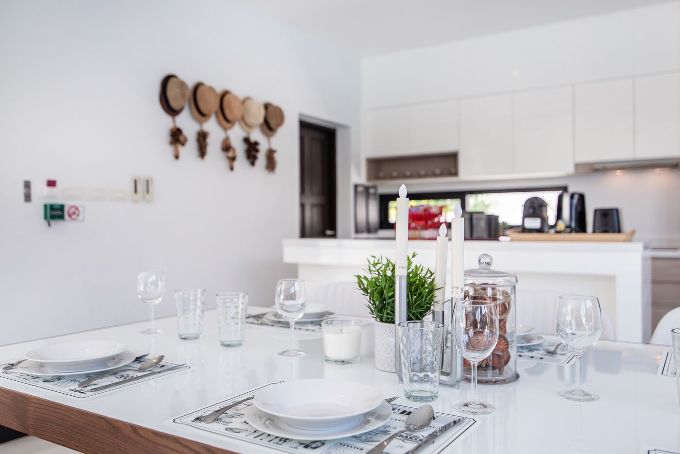 A modern kitchen with white cabinets, a dining table set with plates, glasses, and candles.