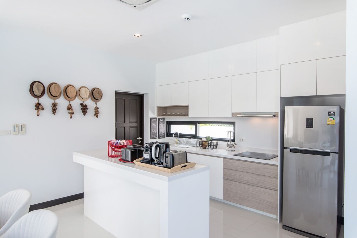 A modern kitchen with white cabinetry, a stainless steel refrigerator, and a coffee station.