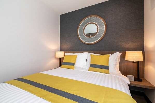 A hotel room with a large bed, two bedside lamps, a round mirror on the wall, and a wooden headboard.