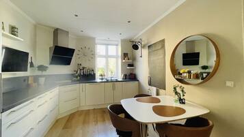 A modern kitchen with white cabinets, a black countertop, and a dining area with a white table and brown chairs.